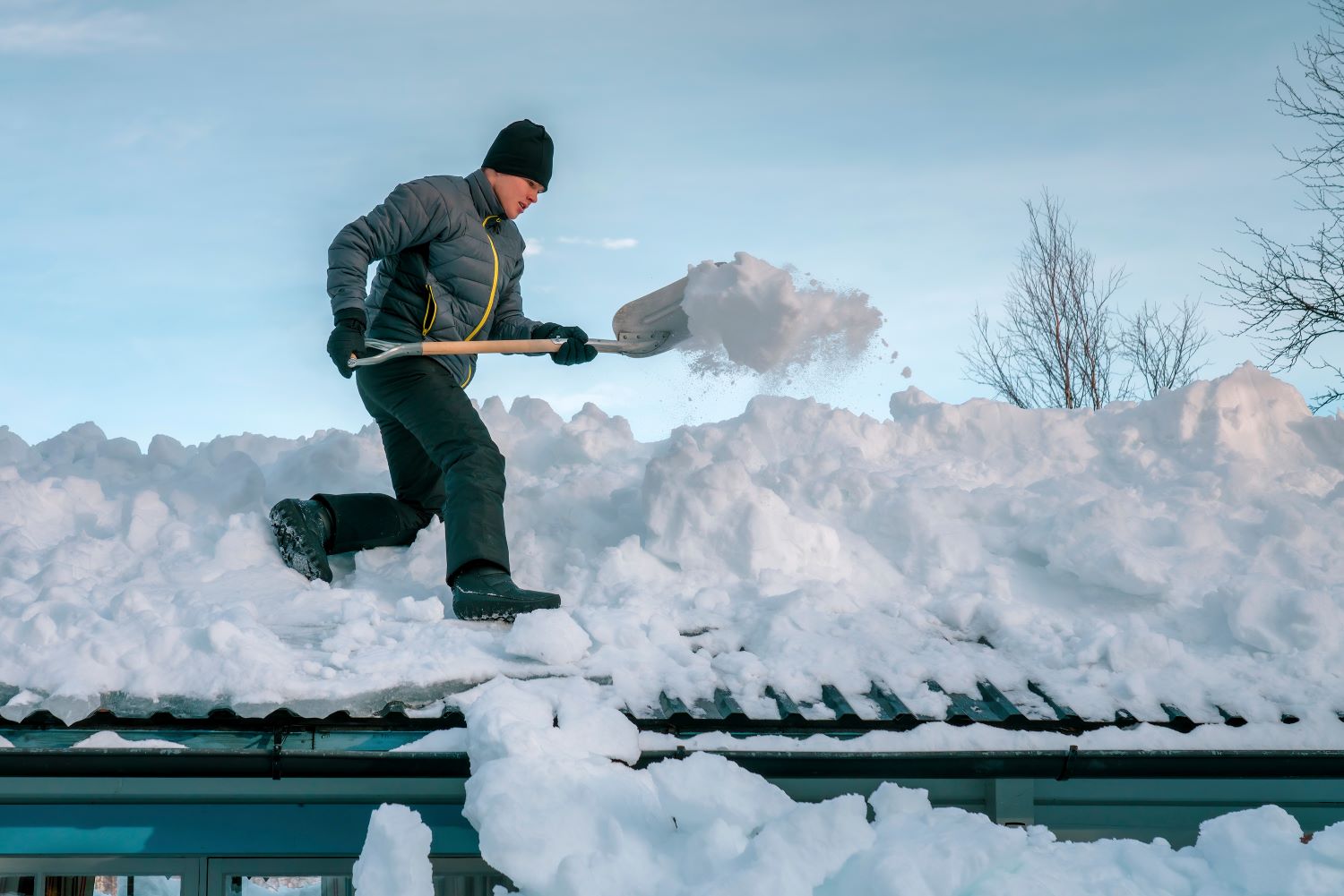 teenager with shovel remove snow from roof of totally snow covered house, cabin in mountains.