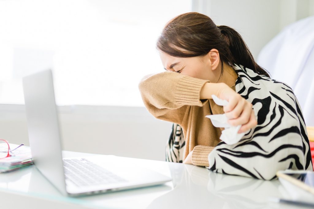 Asian woman sneezing on hinge joints arm at homeWork at homeCoronavirus COVID-19 reducing of risk of spreading the infection by covering nose and mouth when coughing and sneezing with tissue